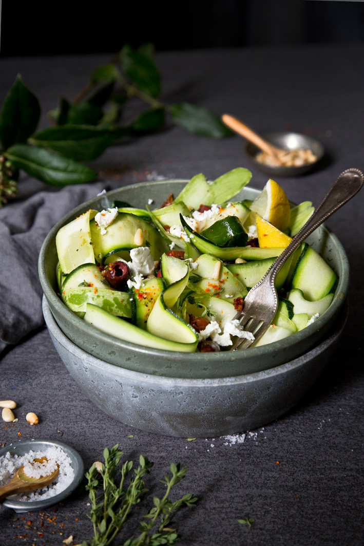 Roher Zucchinisalat mit Feta und Oliven in Schüssel auf dunklem Tisch