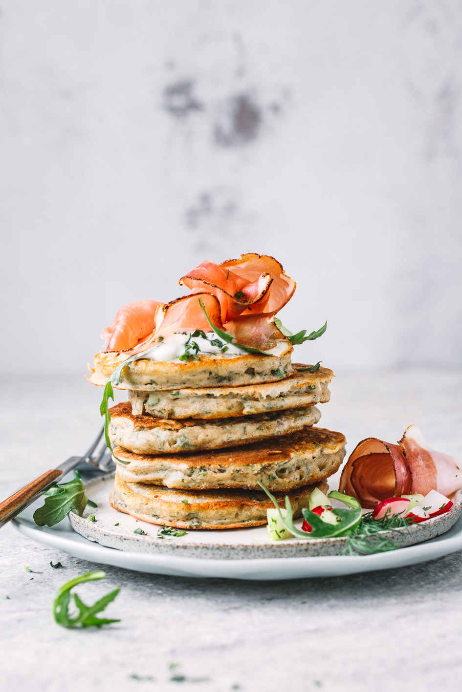 Zucchini-Kräuter-Pancakes übereinandergestapelt mit Speck auf Teller
