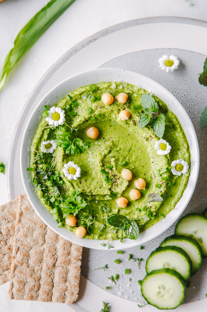 Frühlingskräuter-Hummus Frühlingskräuter-Hummus in Schälchen mit Cracker und Gurken