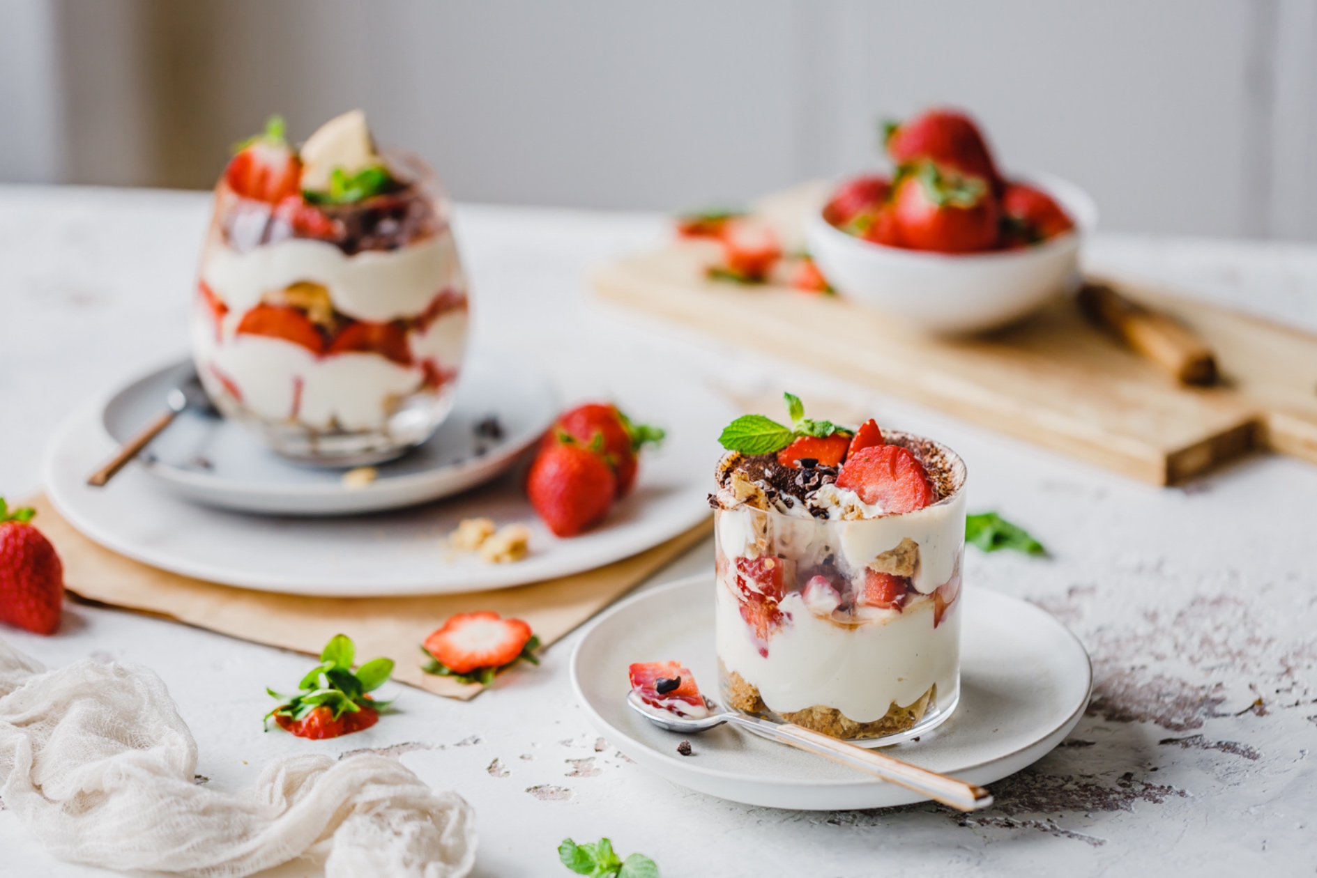 Zwei Gläser veganes Erdbeer-Tiramisu auf Tellern angerichtet
